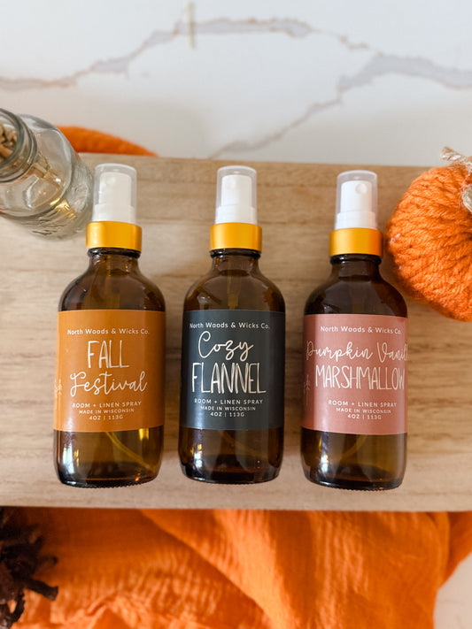 Three bottles of North Woods & Woods Co. diffuser sprays on a wooden surface with pumpkins in the background.