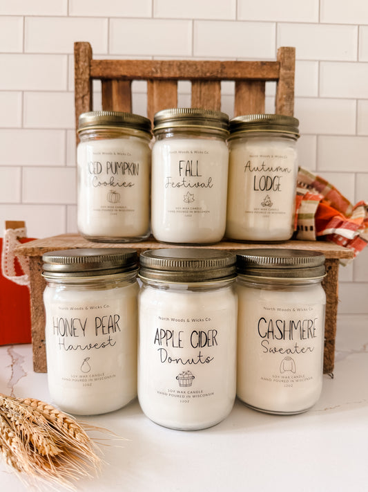 Set of candles with labeled scents on a wooden stand against a tiled wall.